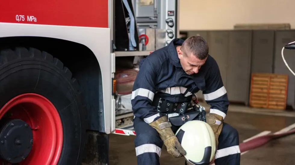 Firefighter sitting on firetruck step looking reflective while staring down at his helmet