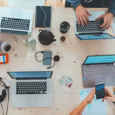 Overhead view of four laptops and two sets of hands at work