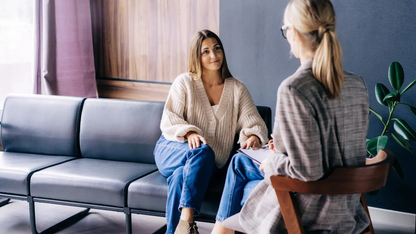 Two females sitting in business casual conversing, one with a clipboard Two females sitting in business casual conversing, one with a clipboard