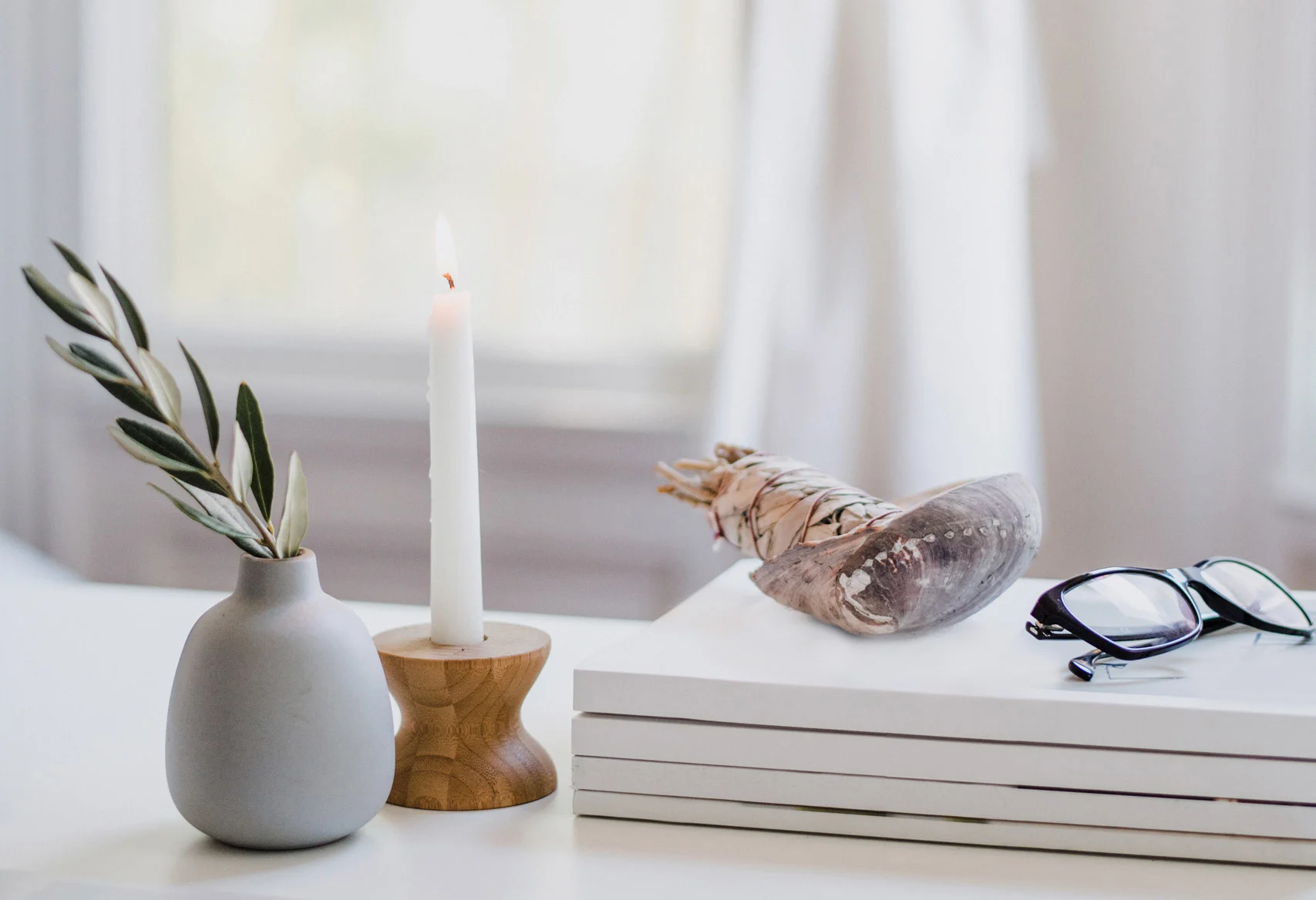 Serene setting of glasses, sage, a candle, and a small plant against white Serene setting of glasses, sage, a candle, and a small plant against white