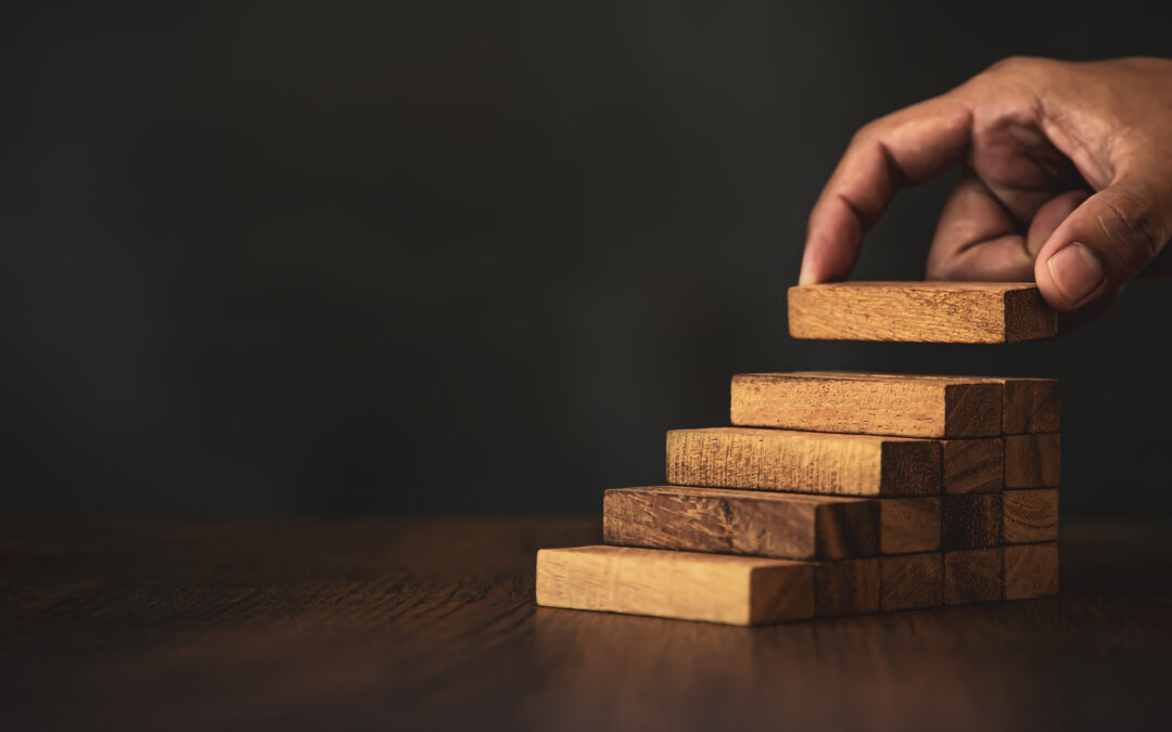 Close-up hand is placing wood block tower stacked in stair step